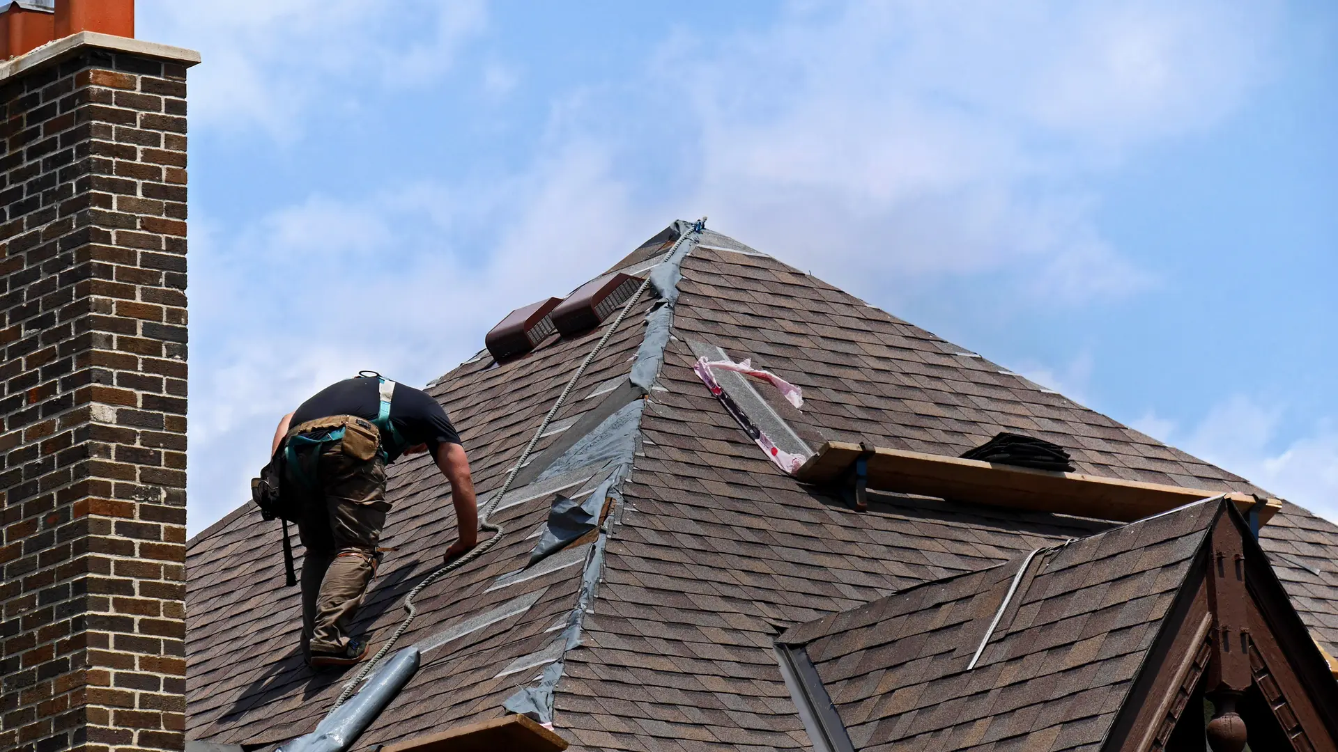 Roofer working on an asphalt shingle roof beside a brick chimney
