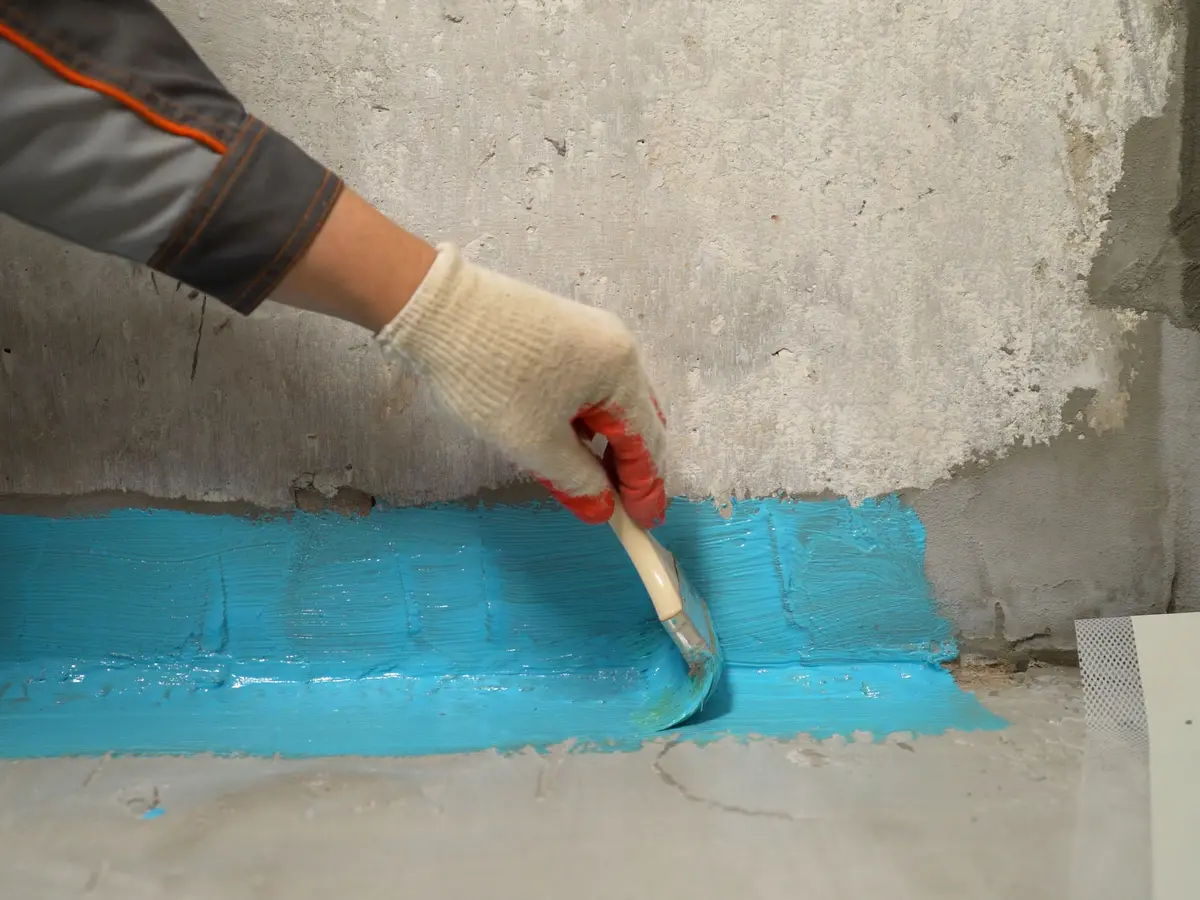 Waterproofing membrane being brushed along an inside wall and floor joint
