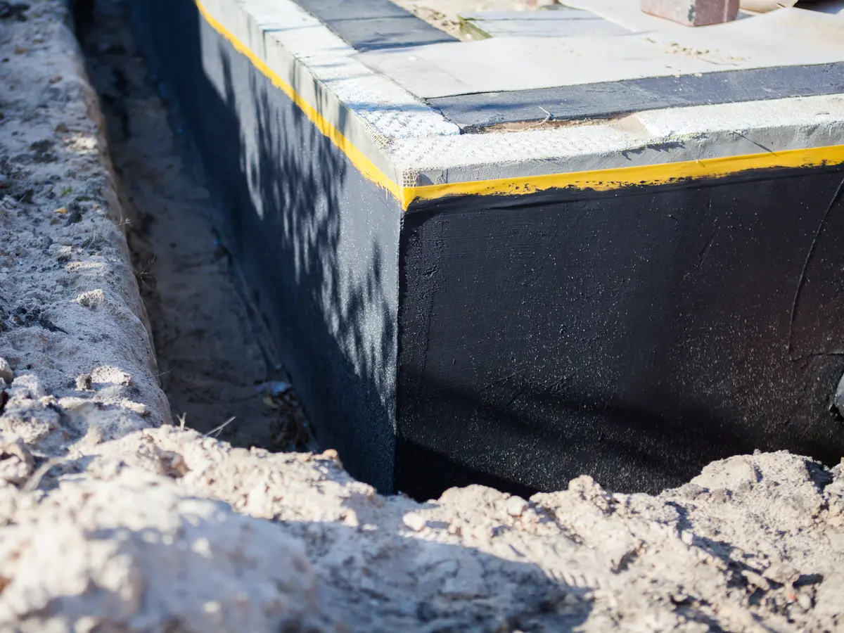 Foundation wall wrapped in a waterproof membrane beside an open trench