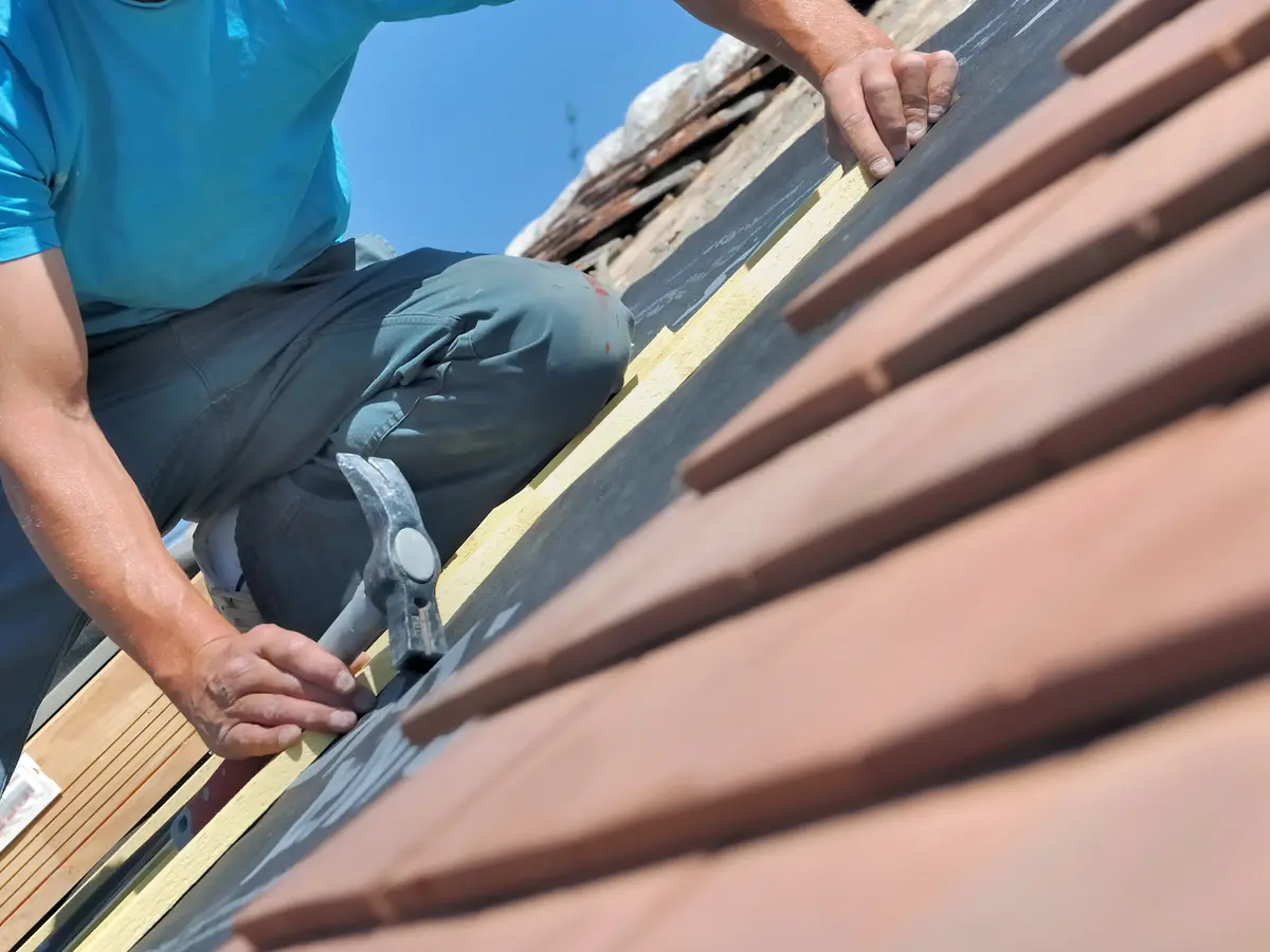 Roofer with a hammer replacing roof covering on a pitched roof