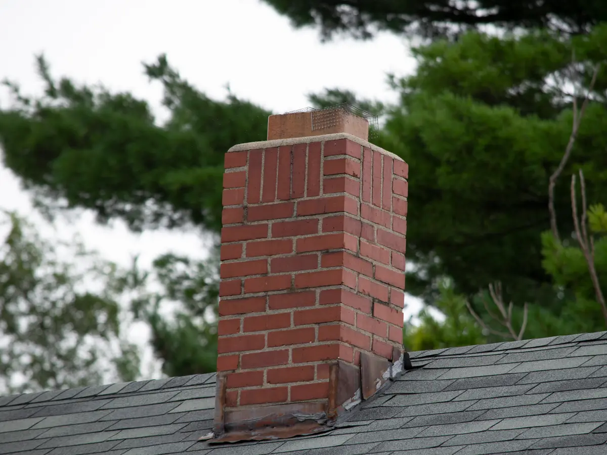 Brick chimney with metal flashing where it meets a shingle roof