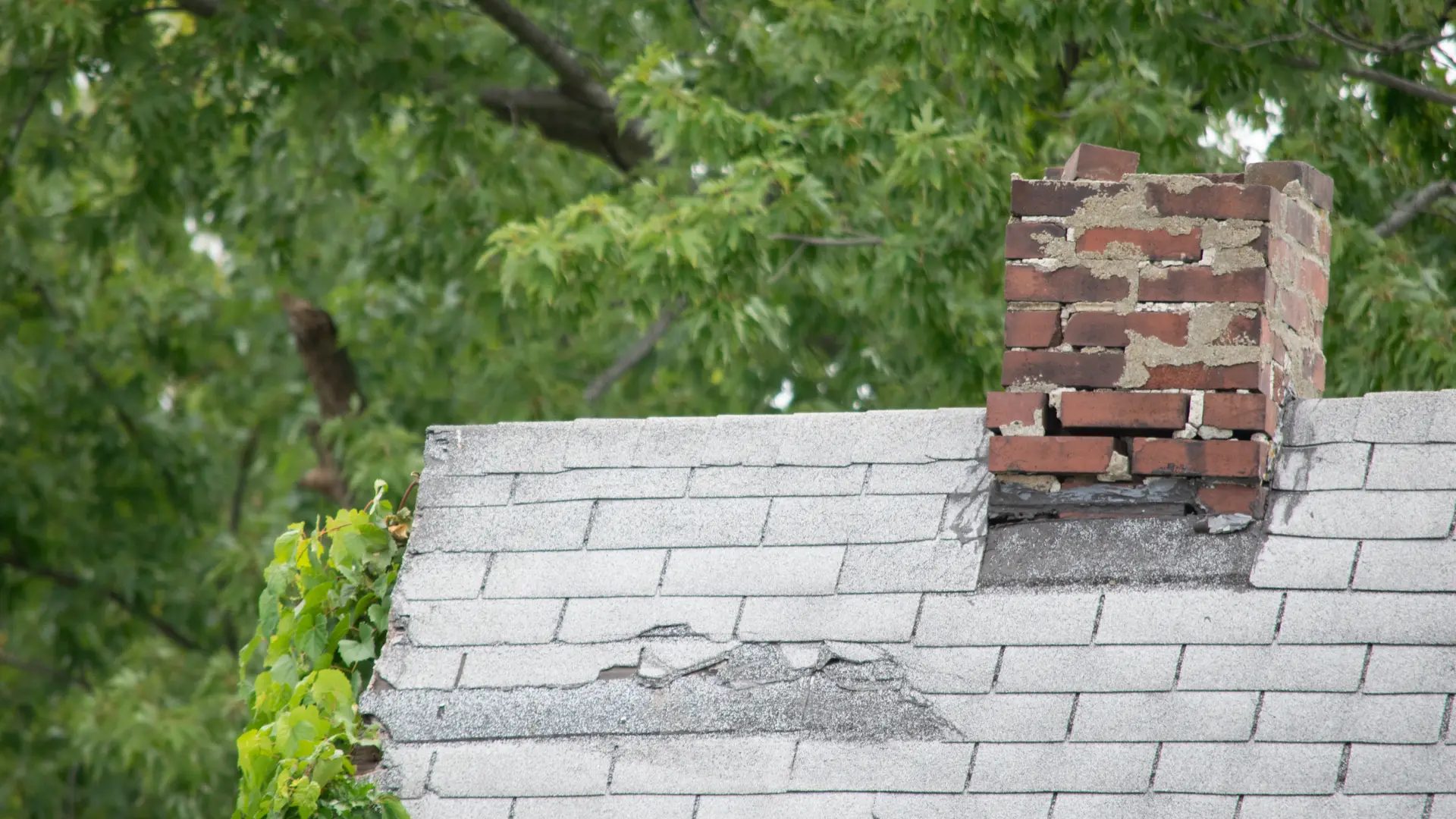Damaged brick chimney with crumbling mortar on a shingle roof