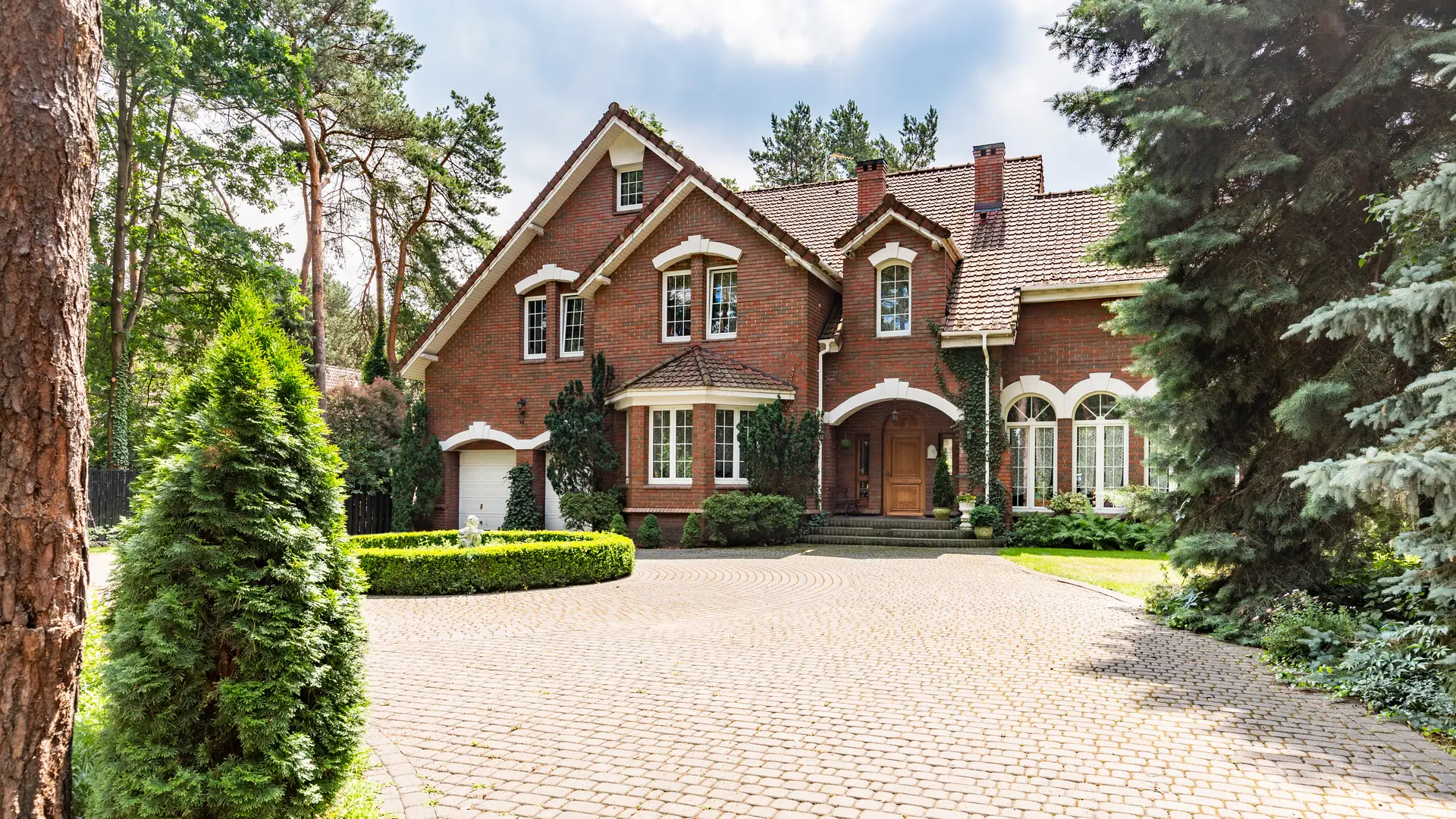 Brick house with a wide interlock driveway and evergreen trees
