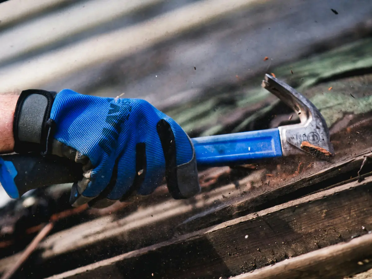 Gloved hand with a hammer at a rotted fascia board