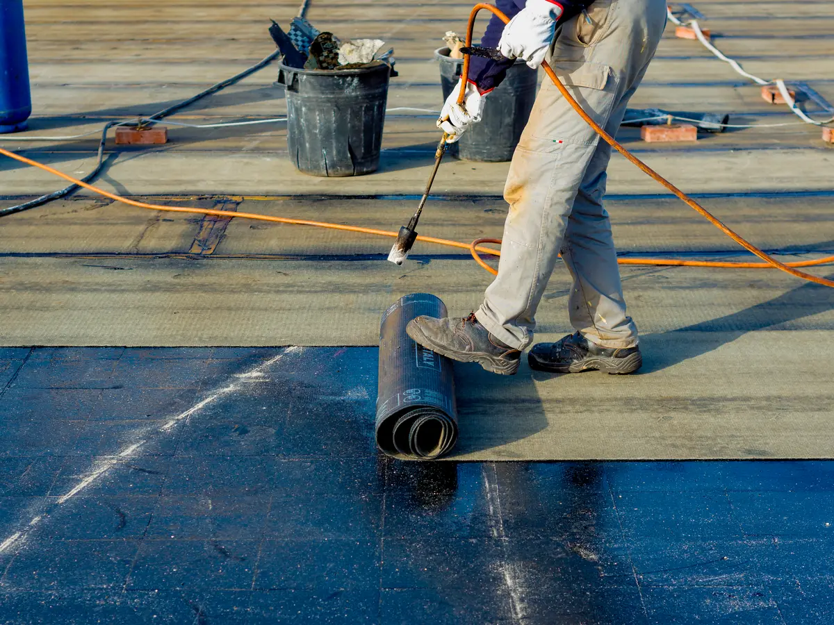 Roofer torching down a roll of modified bitumen membrane on a flat roof