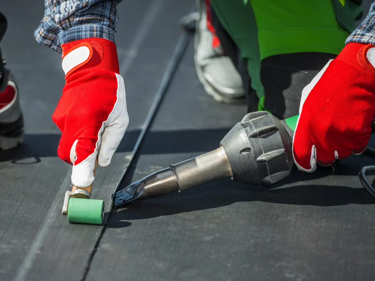 Gloved hands hot-air welding the seam of a flat roof membrane