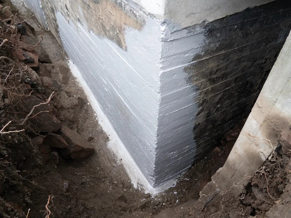 Foundation wall coated with black waterproofing below the finished render