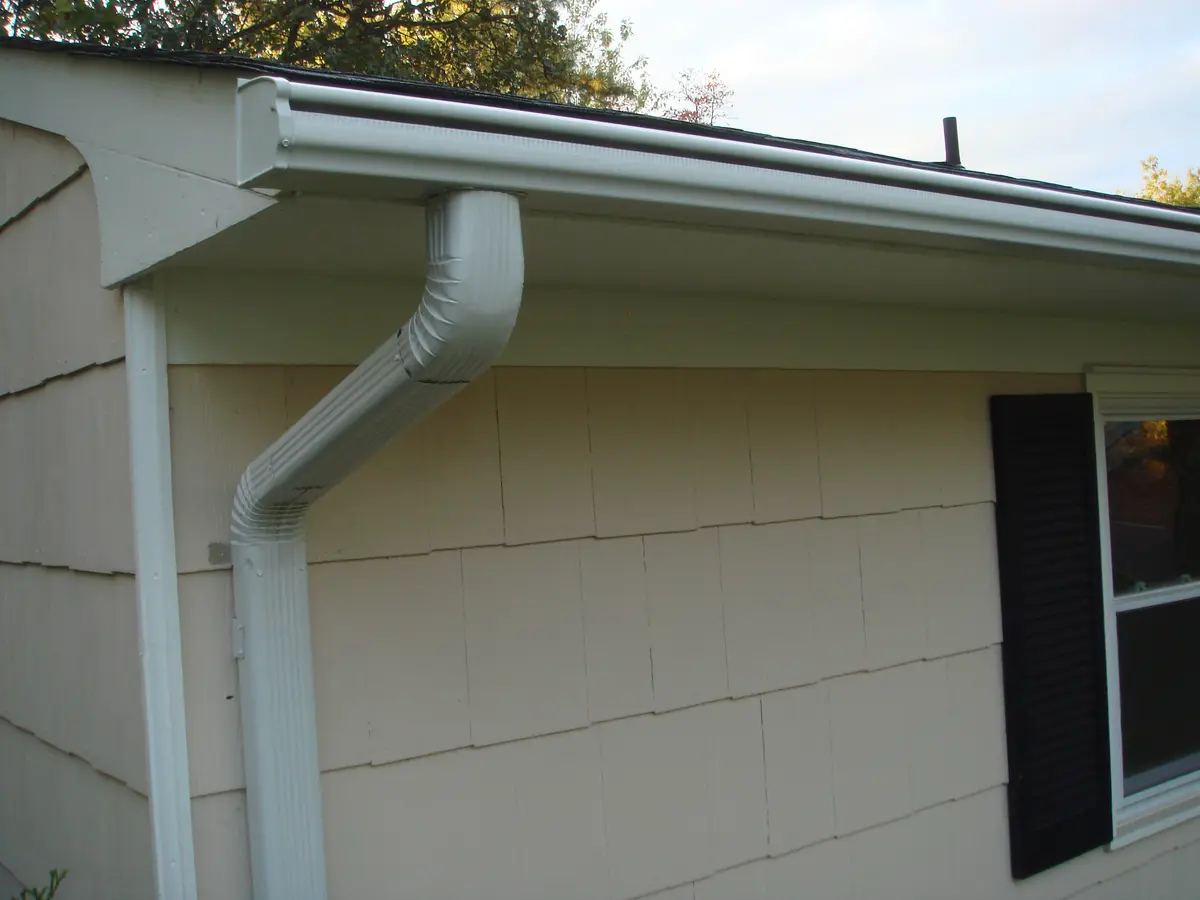 White downspout running down the shingle siding of a house
