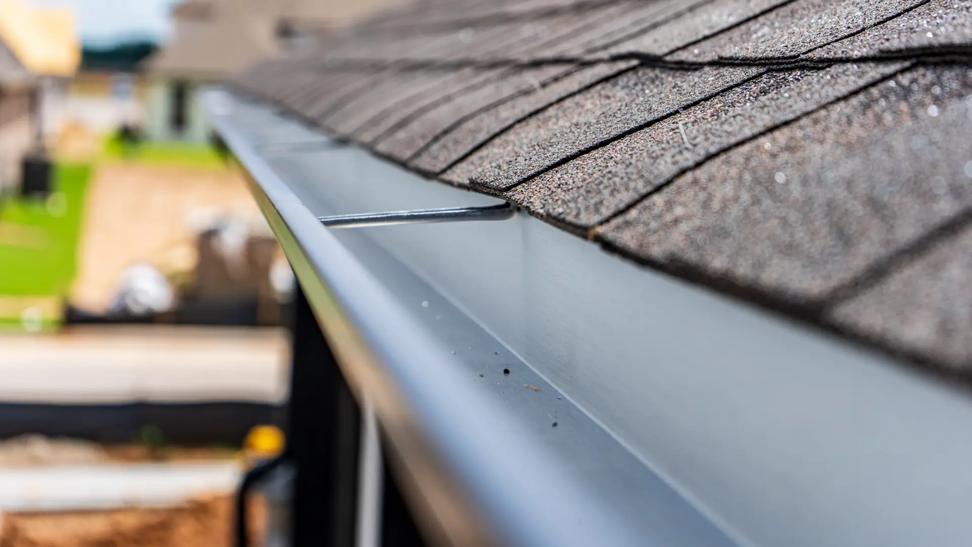 Black eavestrough running along the edge of an asphalt shingle roof