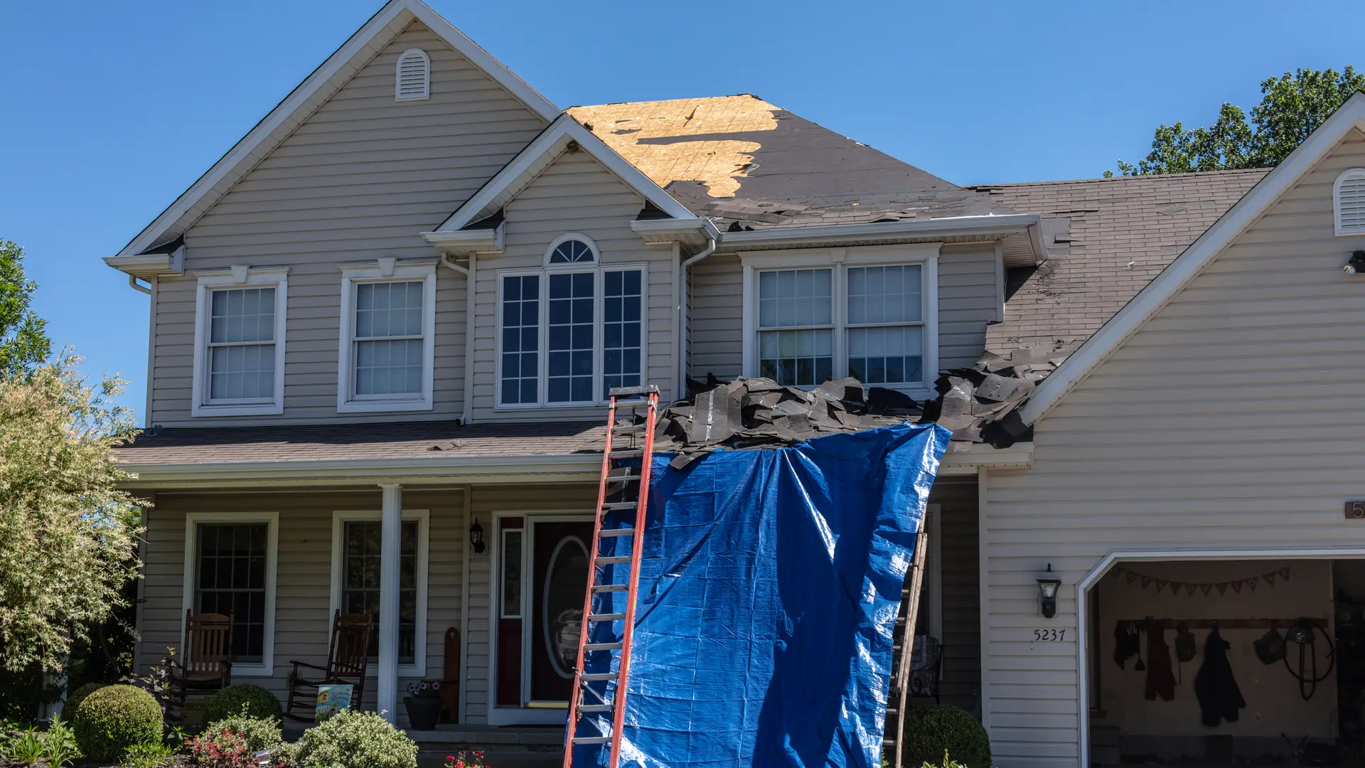 Two-storey house during a roof replacement with a ladder and tarp at the front