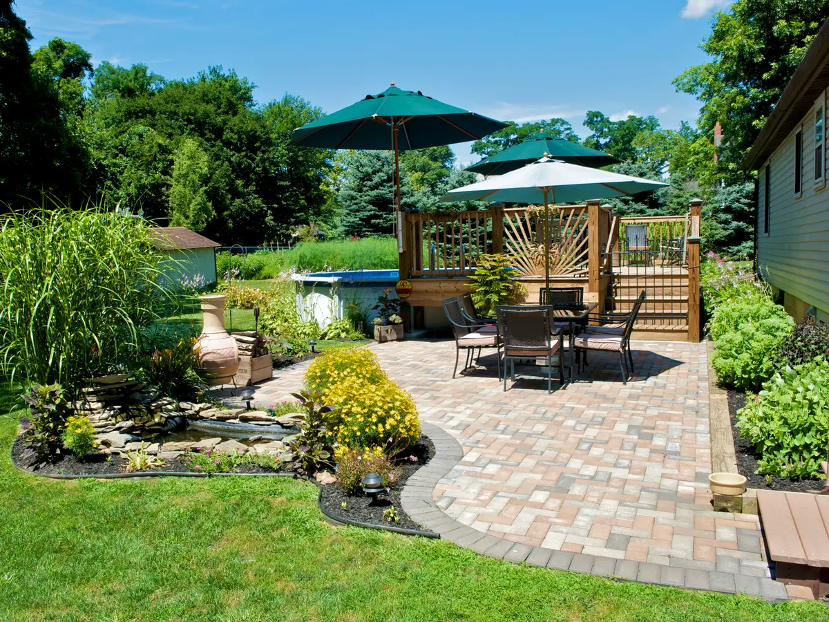 Backyard paver patio with tables and umbrellas beside a garden