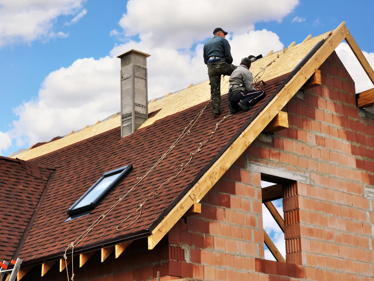 Roofers fitting shingles on the steep roof of a new brick house