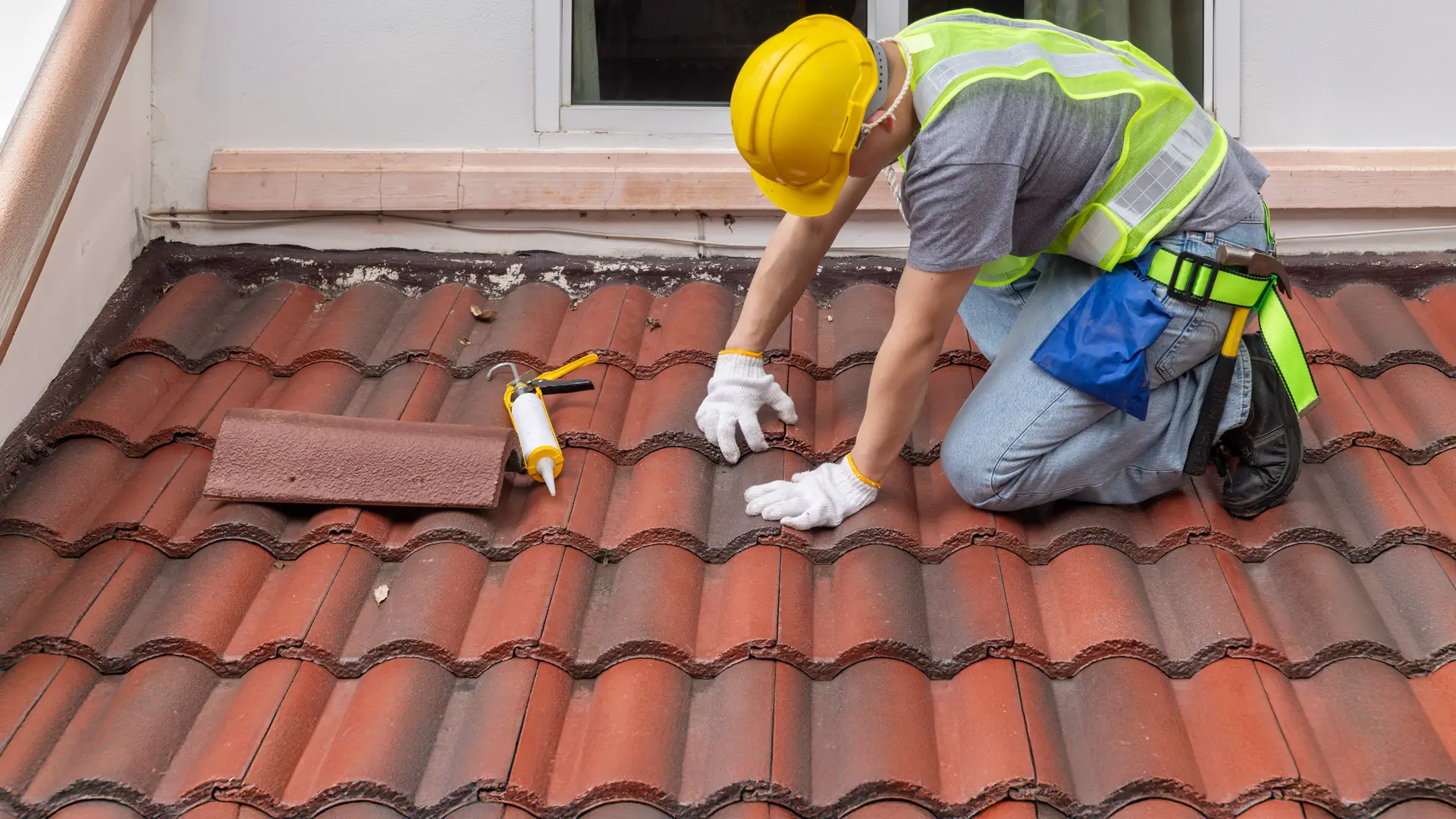 Roofer kneeling on a clay tile roof sealing a replacement tile